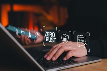 A person types on a laptop keyboard with virtual cybersecurity icons and the words Zero Trust displayed above the keyboard, representing digital security concepts.