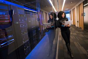 Woman standing in front of computer servers with her laptop in hand.