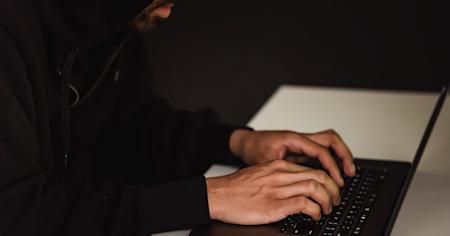 A person in a dark room typing on a laptop.